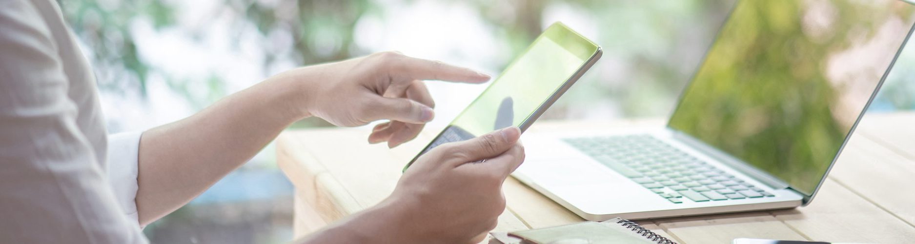 Foto: Arbeitende Person am Smartphone, im Hintergrund ein Laptop