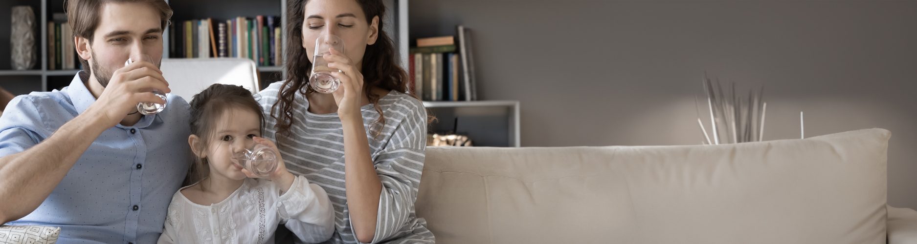 Foto: Eltern trinken mit kleiner Tochter auf dem Sofa ein Glas Wasser