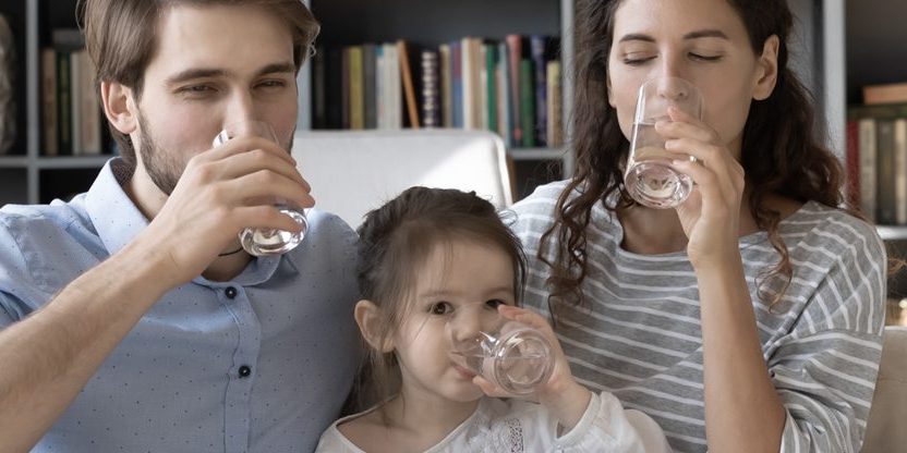 Foto: Eltern trinken mit kleiner Tochter auf dem Sofa ein Glas Wasser